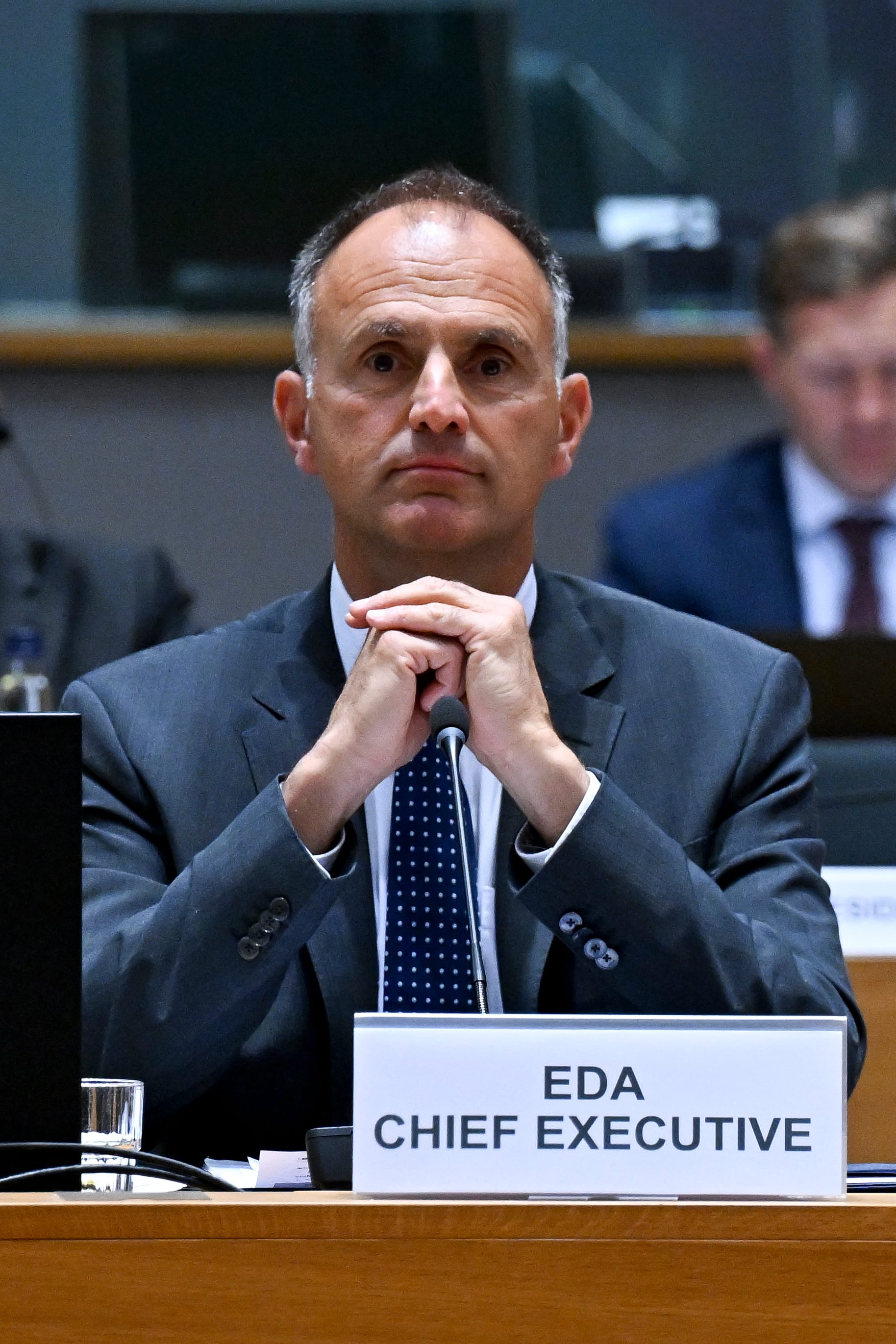 André Denk, jefe ejecutivo de la Agencia Europea de Defensa, con las manos entrelazadas frente a un micrófono en una reunión del Consejo de la UE.