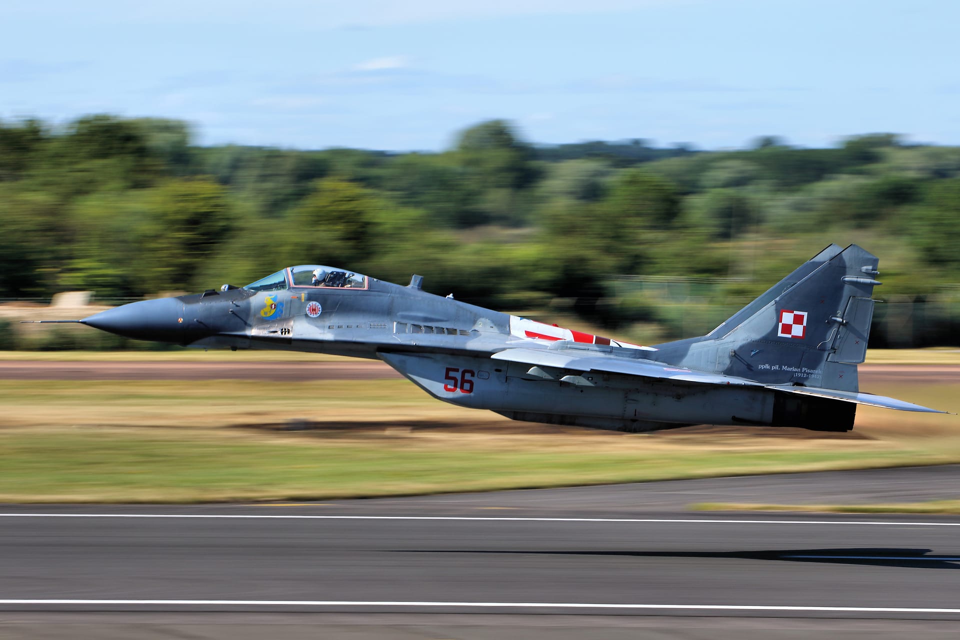 Un caza MiG-29 de la fuerza aérea polaca despega inclinado sobre la pista, con bosque al fondo.