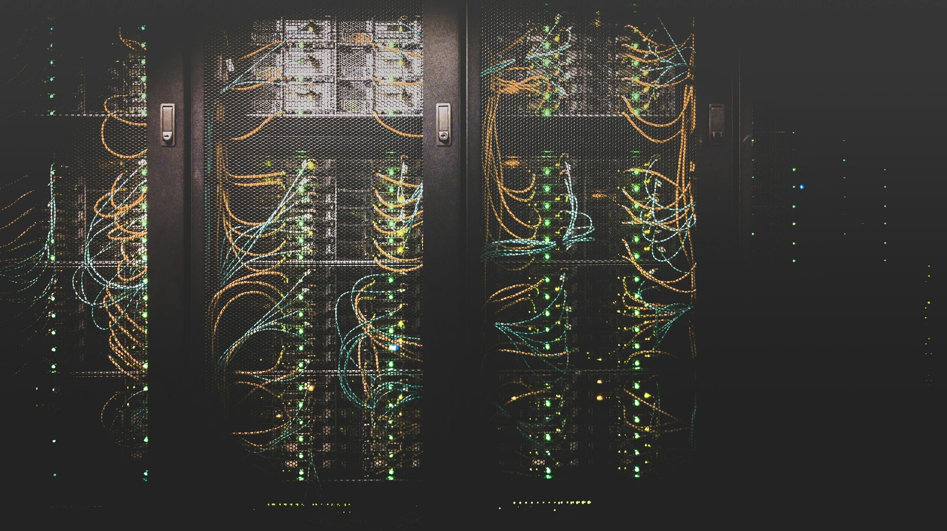 Cables de red color ámbar y verde conectados a racks de servidores en una sala oscura de un centro de datos.