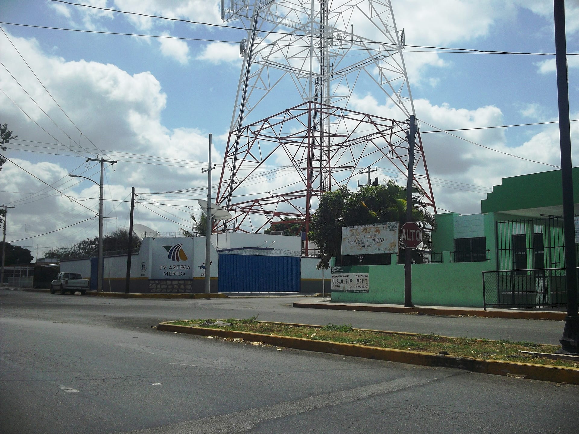 Fachada de las instalaciones de TV Azteca con una torre de transmisión y una antena parabólica detrás.