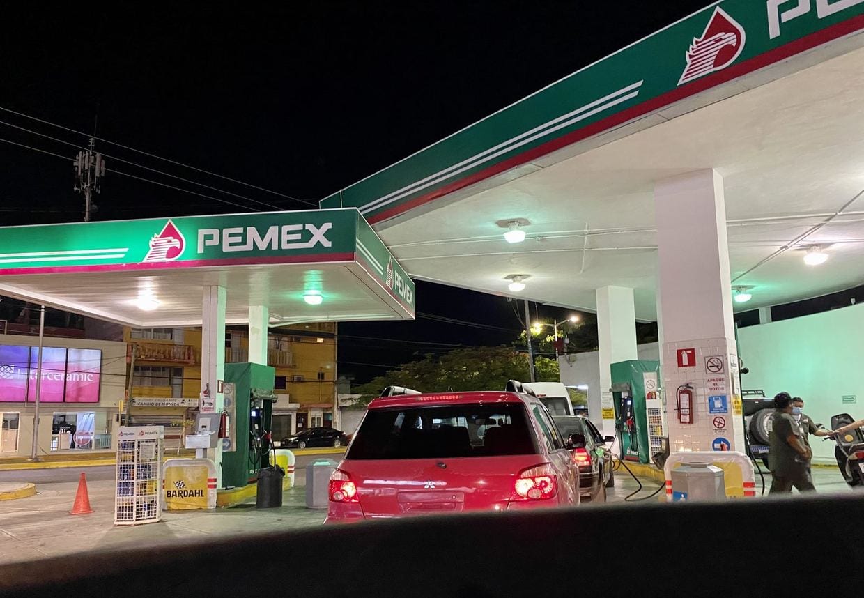 Una gasolinera de Pemex iluminada de noche, con sus bombas y el techo señalizado en rojo y blanco.
