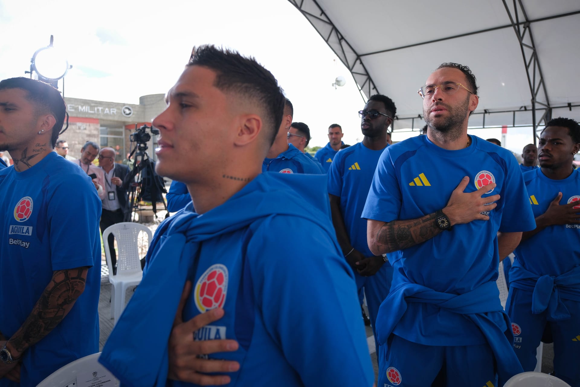 Jugadores de la selección de Colombia, con la mano en el pecho, durante el himno en un acto oficial al aire libre.