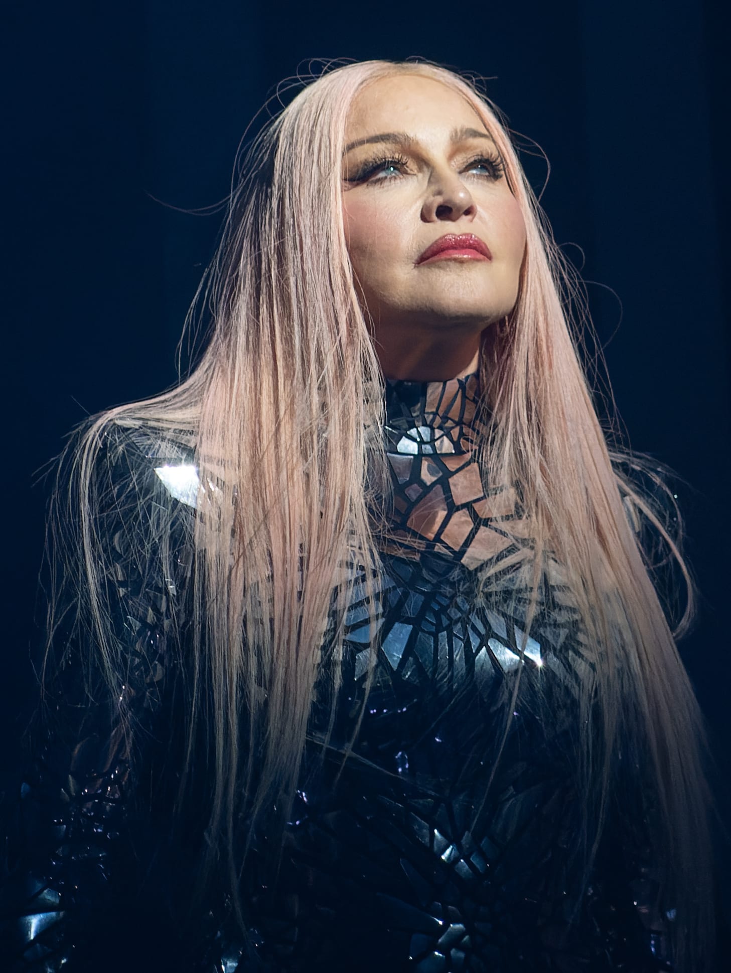 Una mujer rubia con un atuendo escénico oscuro se presenta sobre un escenario iluminado.