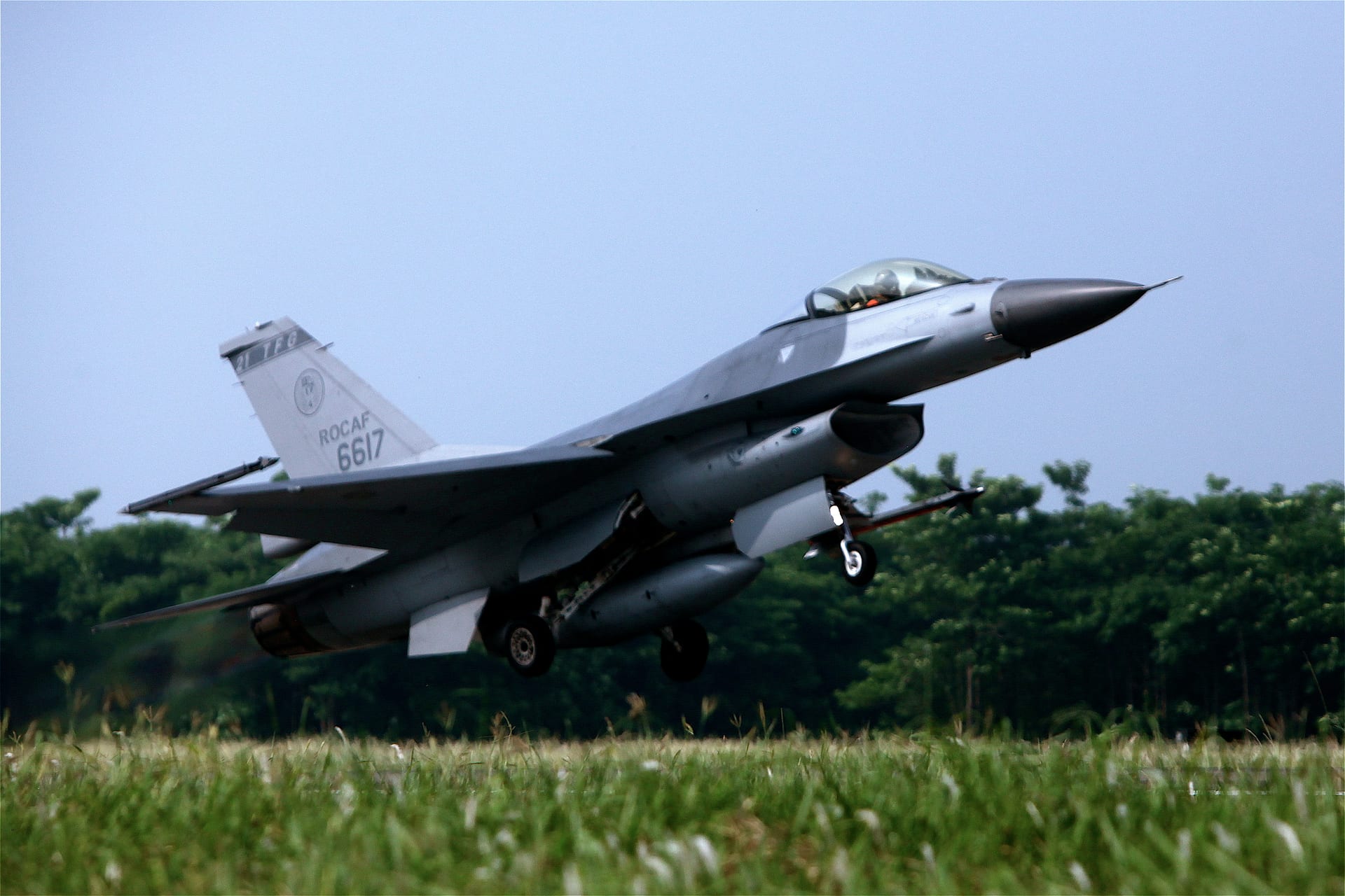 Un caza F-16 con matrícula de la fuerza aérea taiwanesa despega de una pista bordeada de árboles.