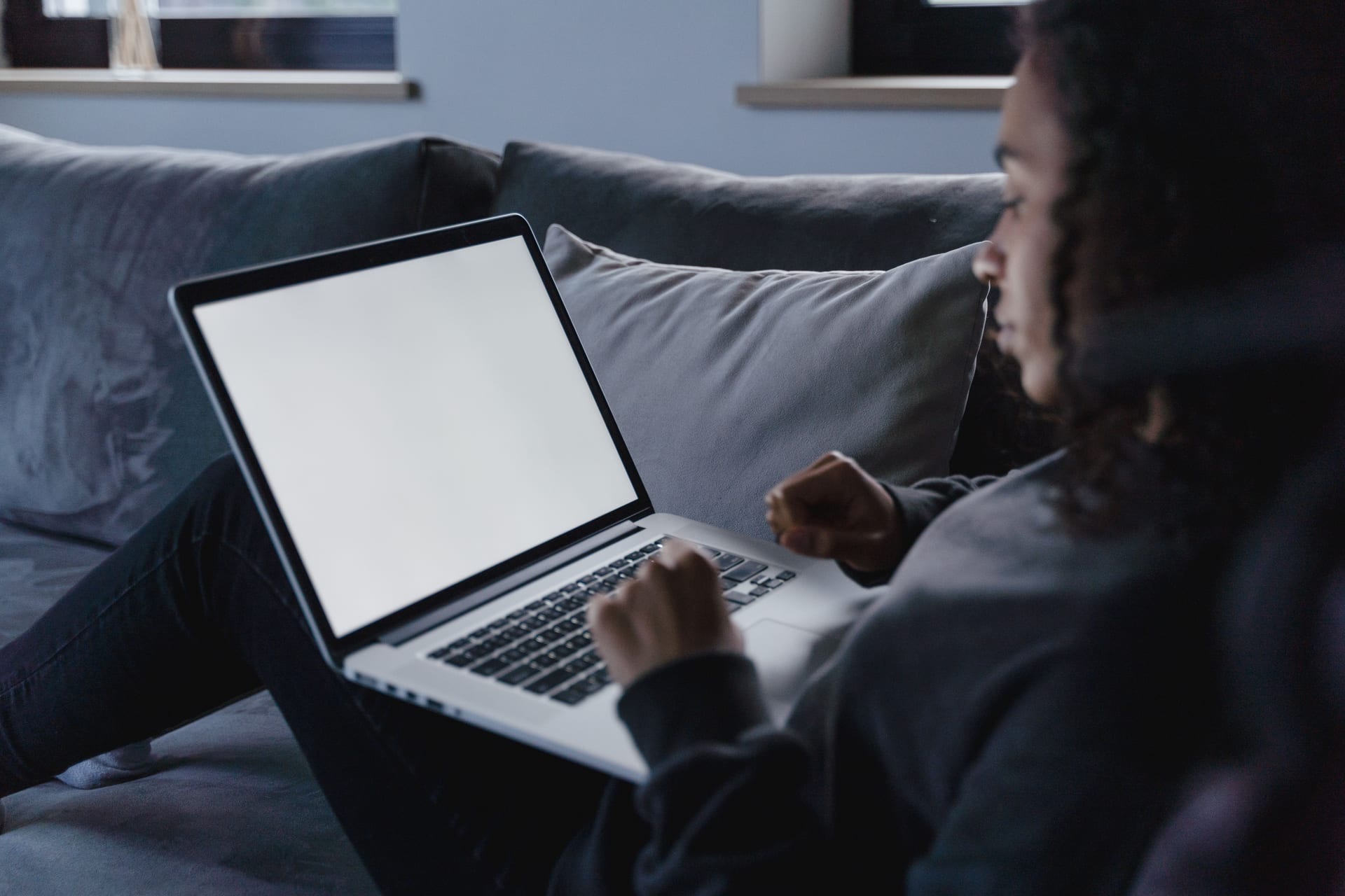 Una mujer sentada en un sillón mira fijamente la pantalla de su laptop en una sala de estar.