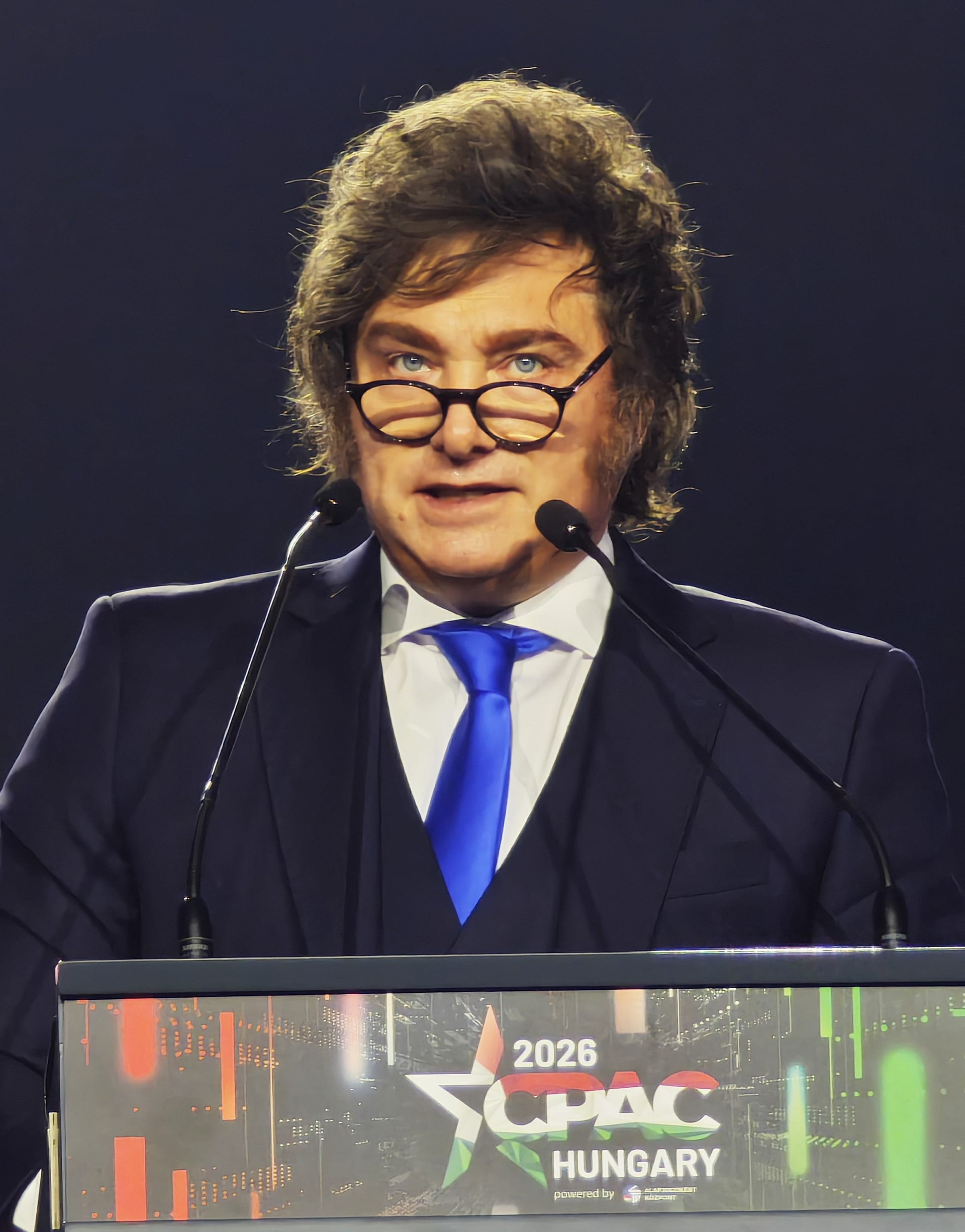 Javier Milei habla frente a dos micrófonos en un podio con el rótulo de un foro internacional detrás.
