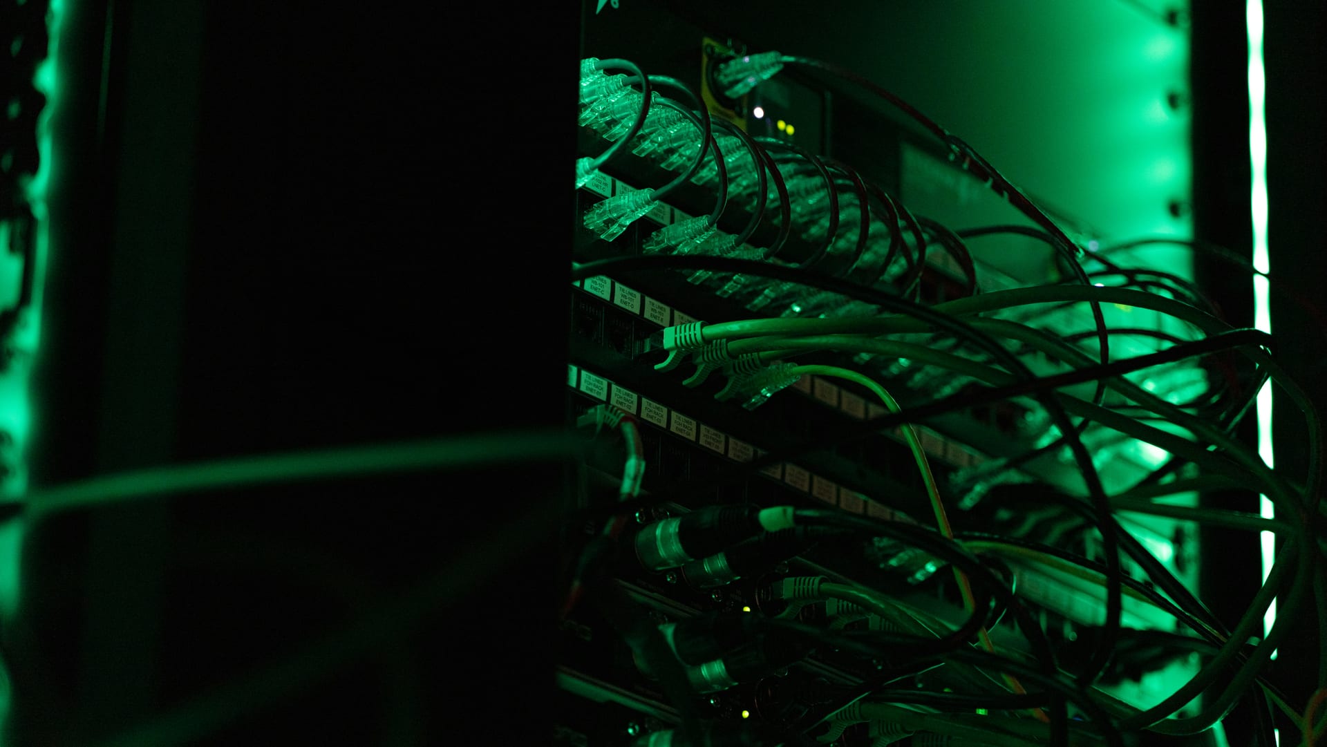 Un bastidor de red con decenas de cables ethernet conectados a switches, iluminado con luz verde.