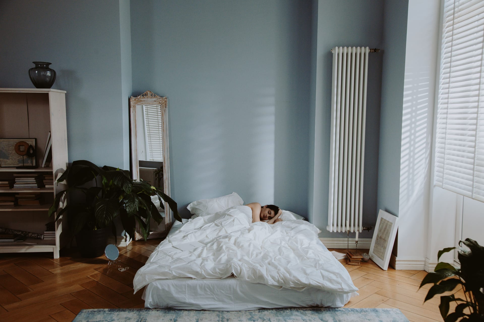 Una persona duerme de lado en una cama con ropa de cama clara, junto a una ventana con luz natural suave.
