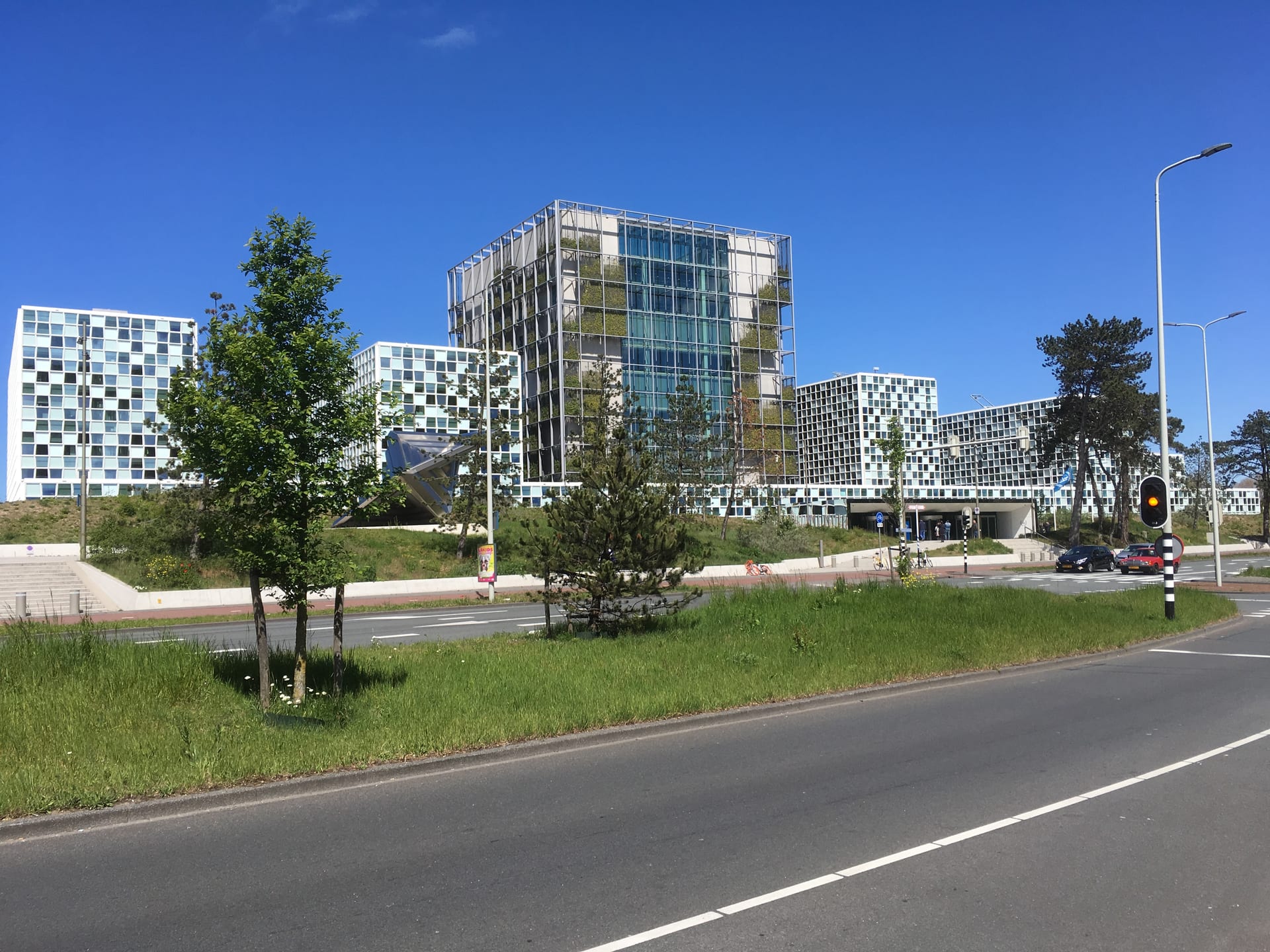 Conjunto de edificios modernos con fachadas de vidrio y paneles junto a una calle con autos, bajo un cielo despejado.