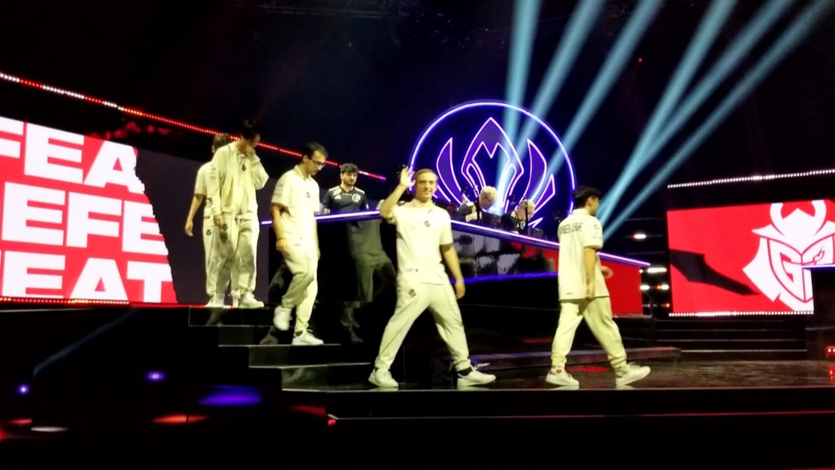 Varios jugadores con uniforme blanco bajan por una escalinata de un escenario iluminado con haces de luz azul.