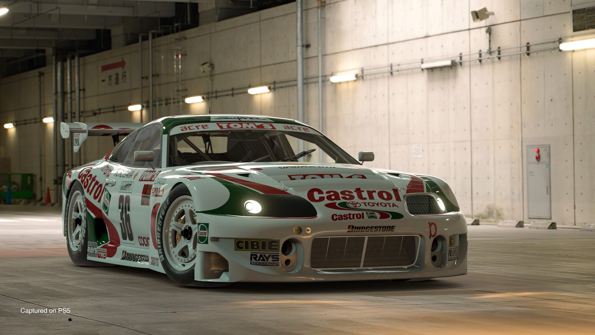 Un auto de carreras blanco con franjas rojas y verdes y patrocinio de Castrol, estacionado en un garaje.