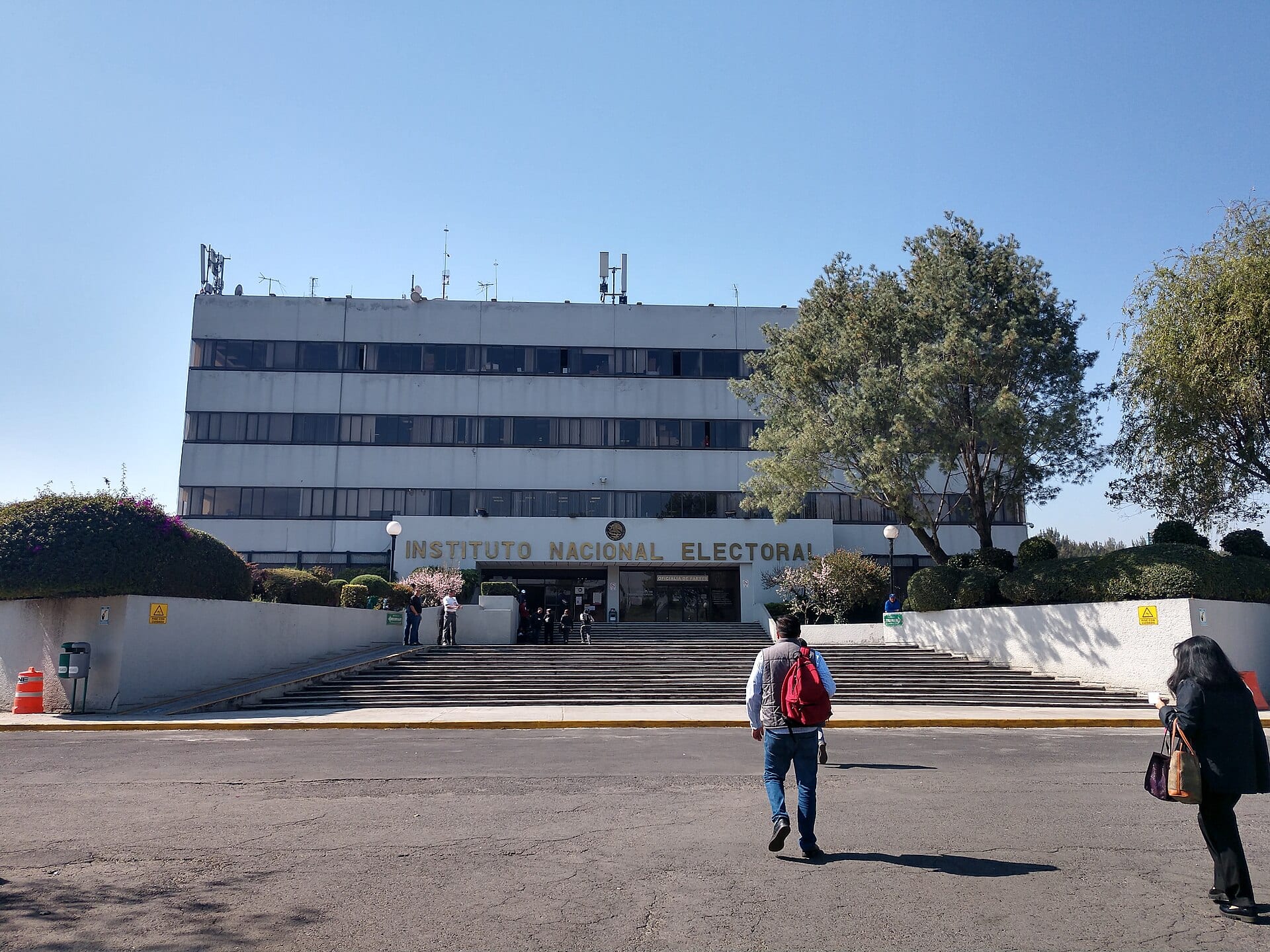 Fachada de un edificio institucional de varios niveles con el letrero Instituto Nacional Electoral y una plaza al frente.