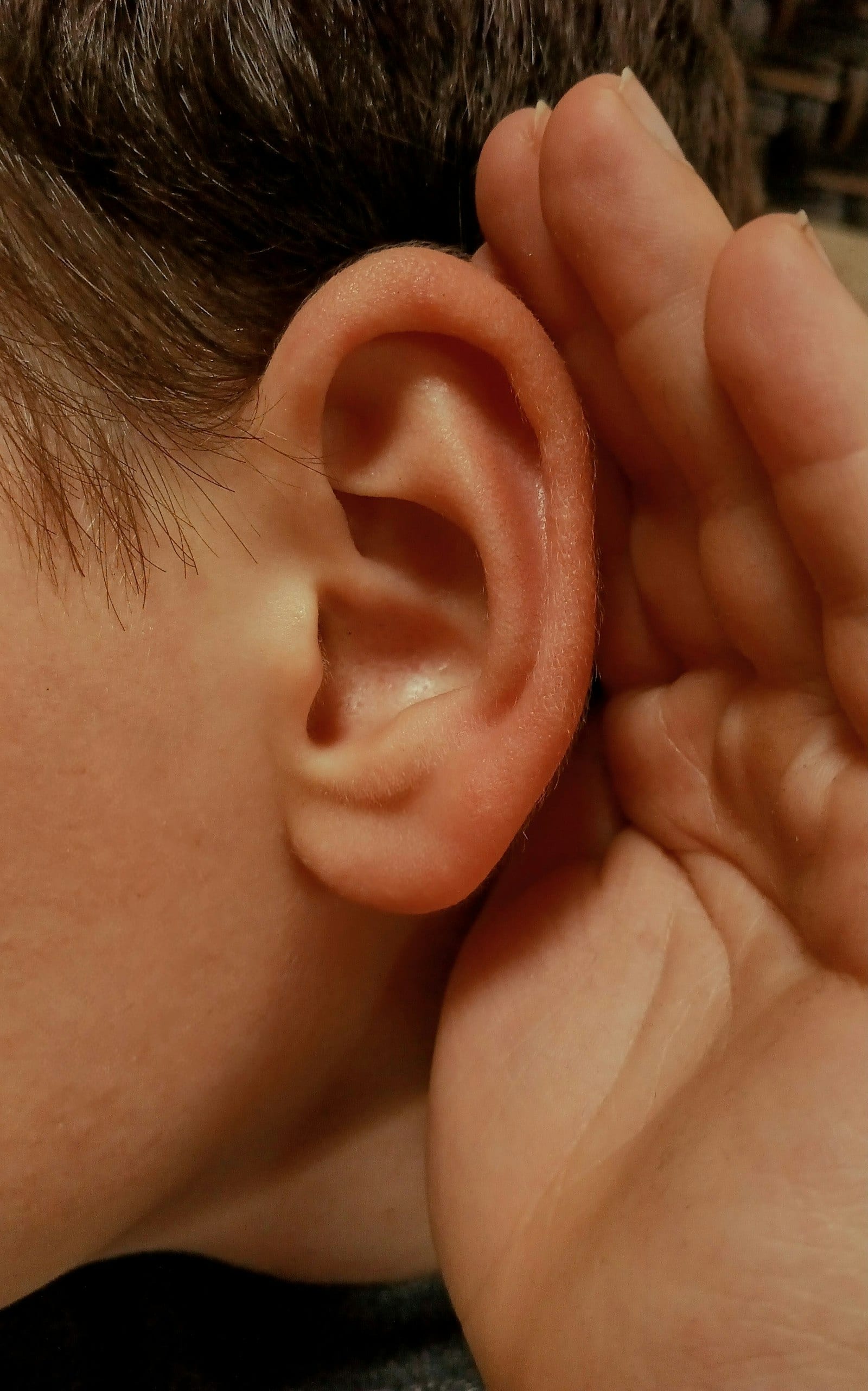 Un primer plano de una oreja mientras una mano se acerca a ella en un gesto de escuchar con atención.