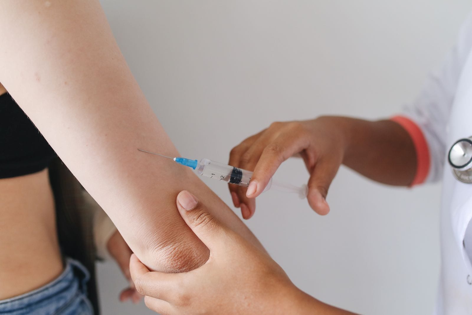 Un profesional de salud sostiene una jeringa junto al brazo de una persona, antes de aplicar una inyección.