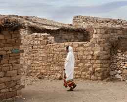 Una mujer envuelta en un manto blanco camina junto a un muro de piedra en una aldea rural del norte de Etiopía.