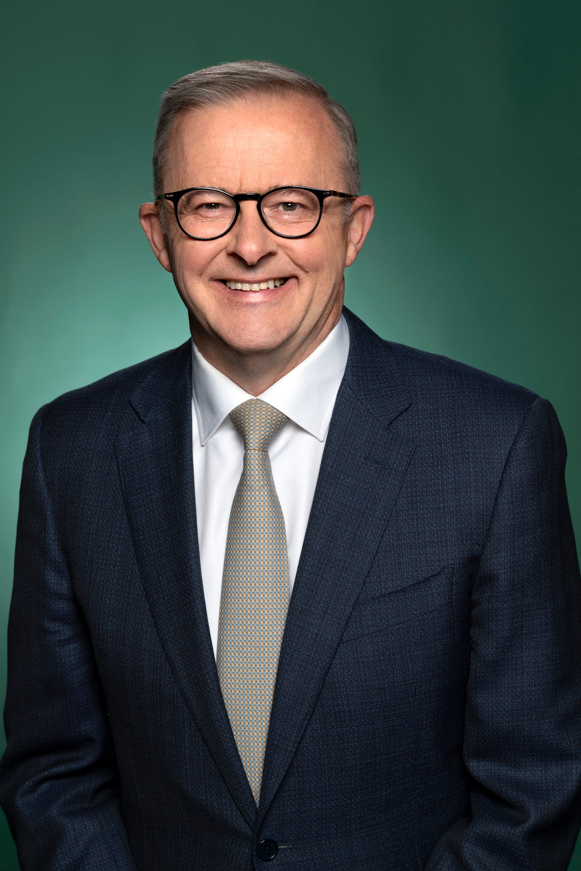 Anthony Albanese sonríe con los brazos cruzados, de traje azul oscuro y corbata clara, ante un fondo verde.