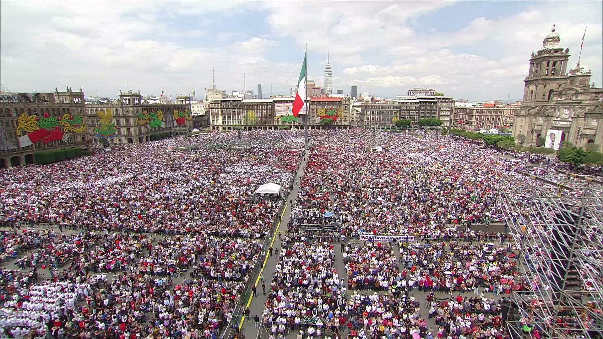 Vista aérea del Zócalo de la Ciudad de México lleno de gente, con la bandera monumental al centro y la Catedral a la derecha.