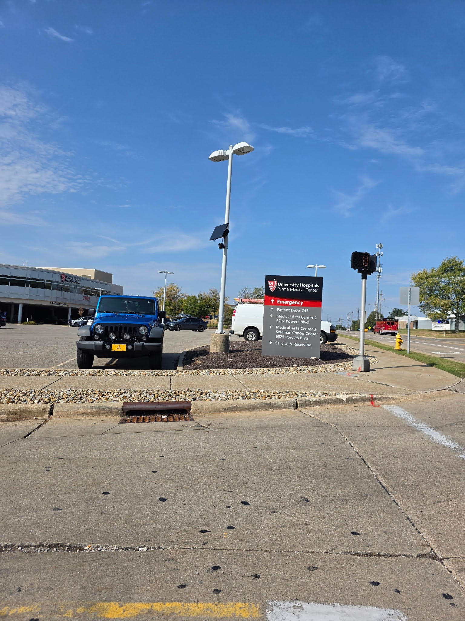Una cámara lectora de placas con panel solar, fijada a un poste blanco en la entrada de un estacionamiento.