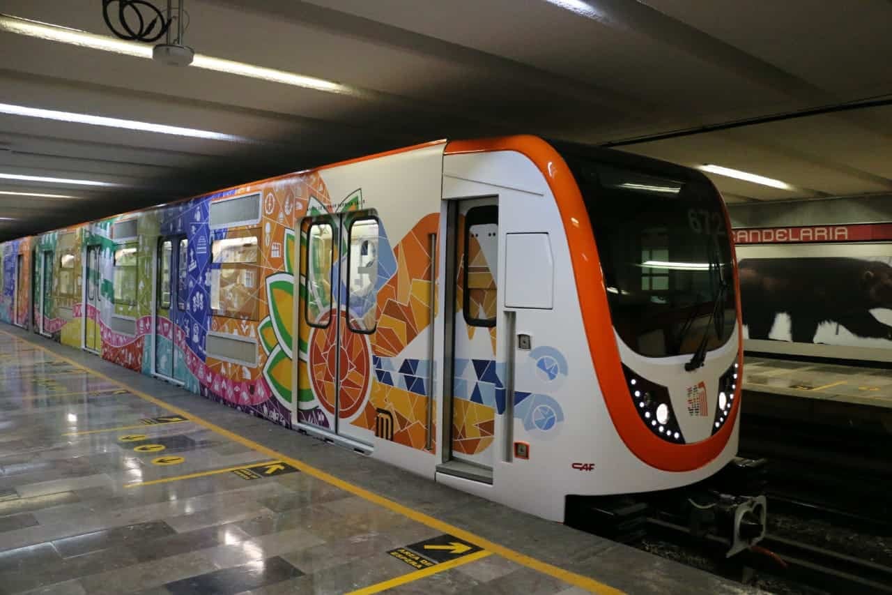 Un tren del Metro con vagones decorados en colores llega a una estación subterránea con andén de mármol.