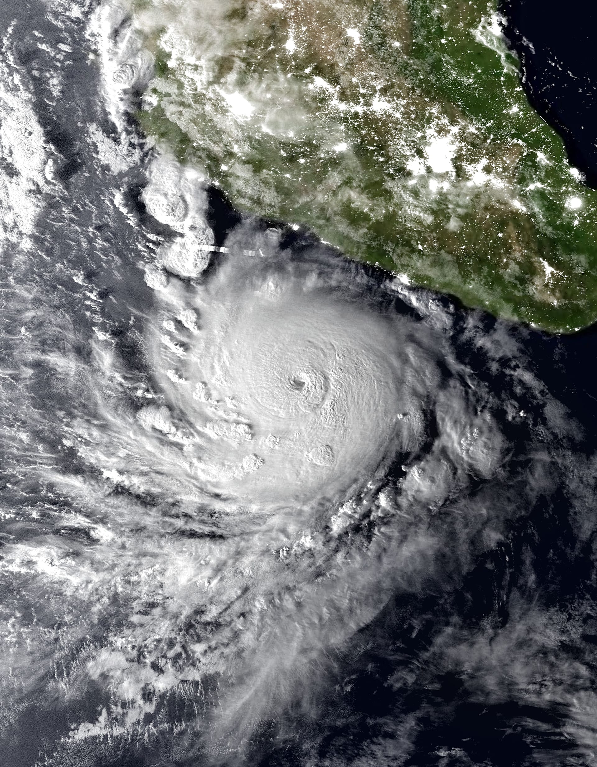 Vista satelital nocturna de un huracán con un ojo circular bien definido frente a una costa iluminada por luces de ciudad.