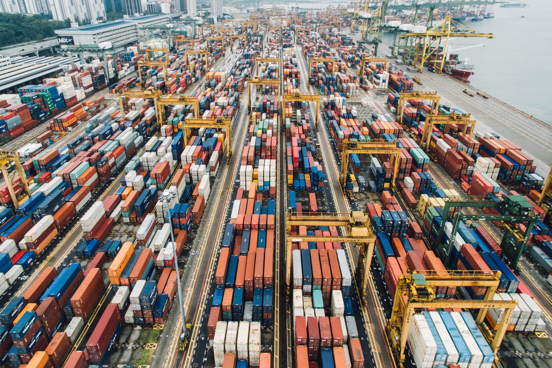 Vista aérea de miles de contenedores de carga apilados en una terminal portuaria, con grúas amarillas entre los pasillos.