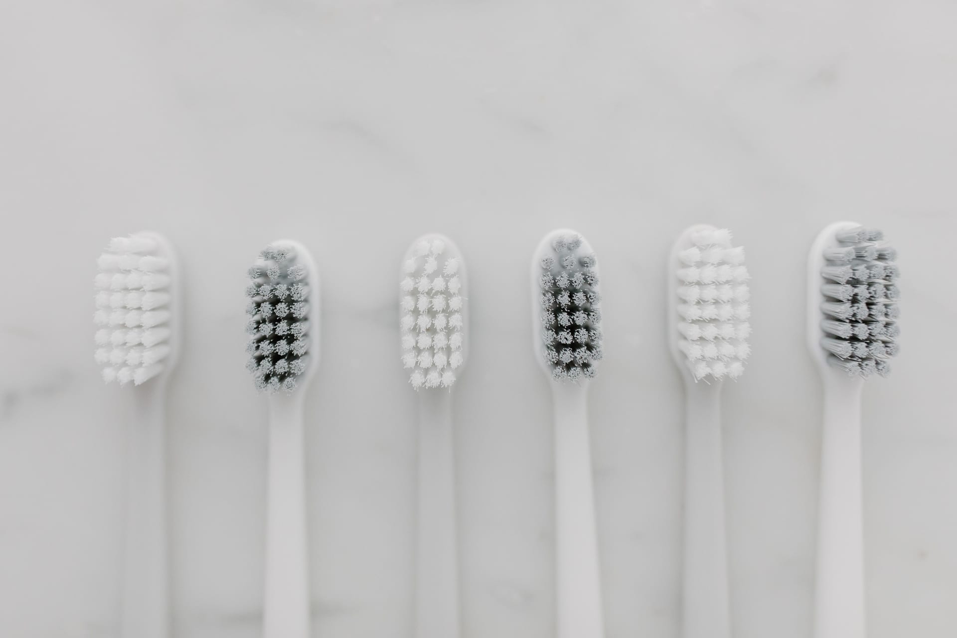 Seis cepillos de dientes blancos alineados en vista cenital sobre una superficie de mármol.