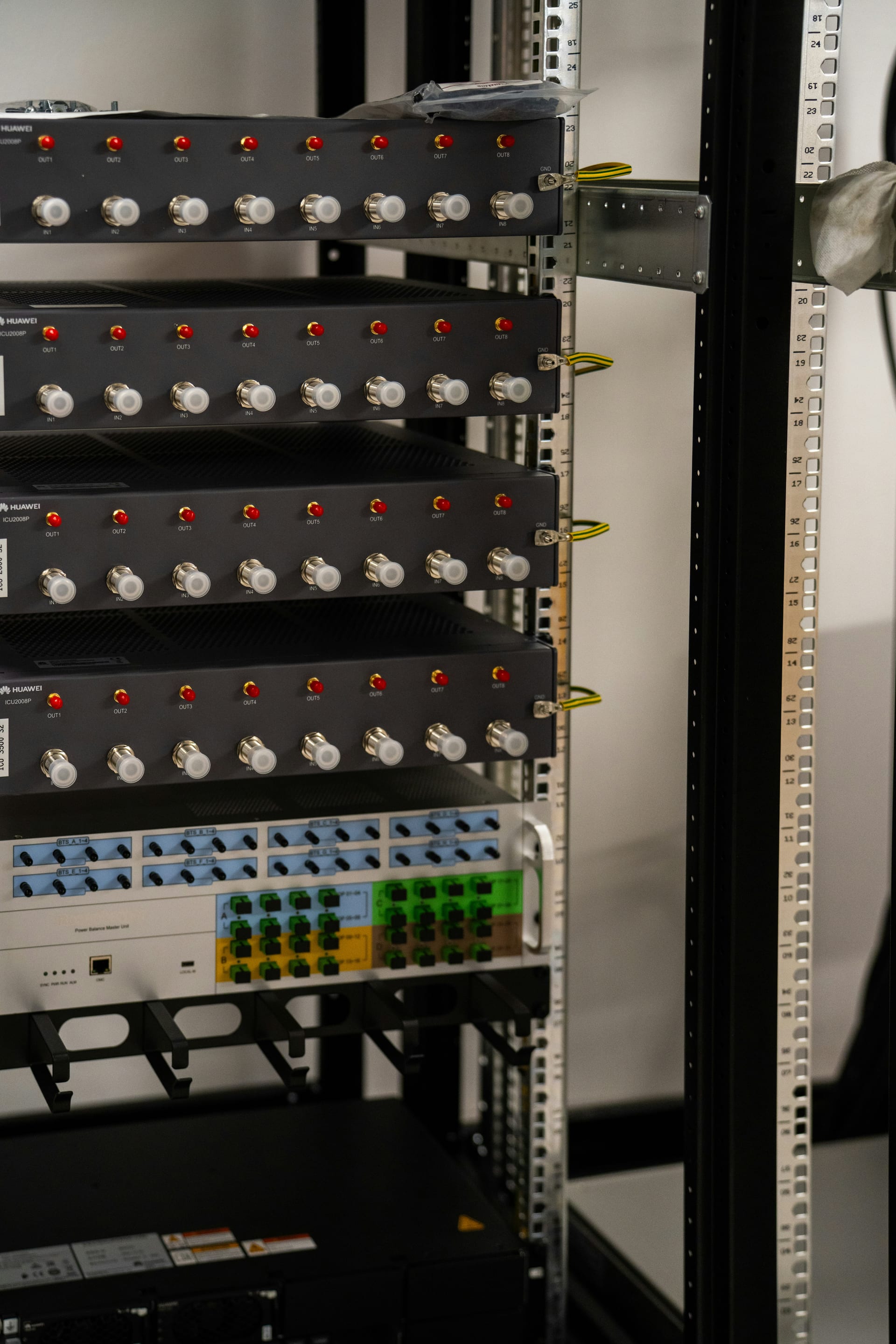Un rack metálico con paneles de equipo de telecomunicaciones marca Huawei, con conectores rojos y blancos etiquetados IN y OUT.