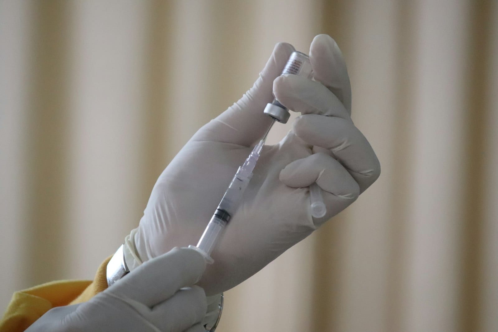 Un par de manos con guantes de látex prepara una jeringa a partir de un vial pequeño.