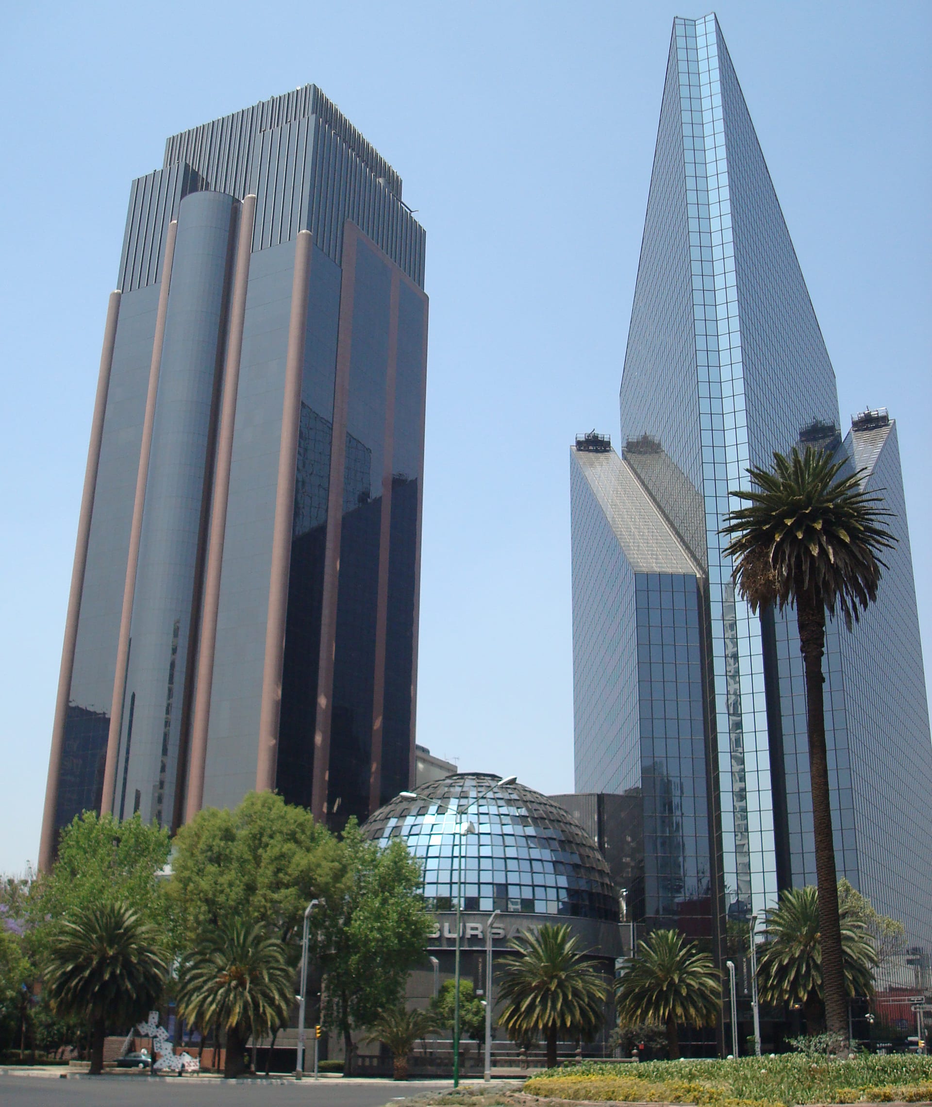 El domo de cristal de la Bolsa Mexicana de Valores, con dos rascacielos de vidrio detrás, un día despejado en Paseo de la Reforma.