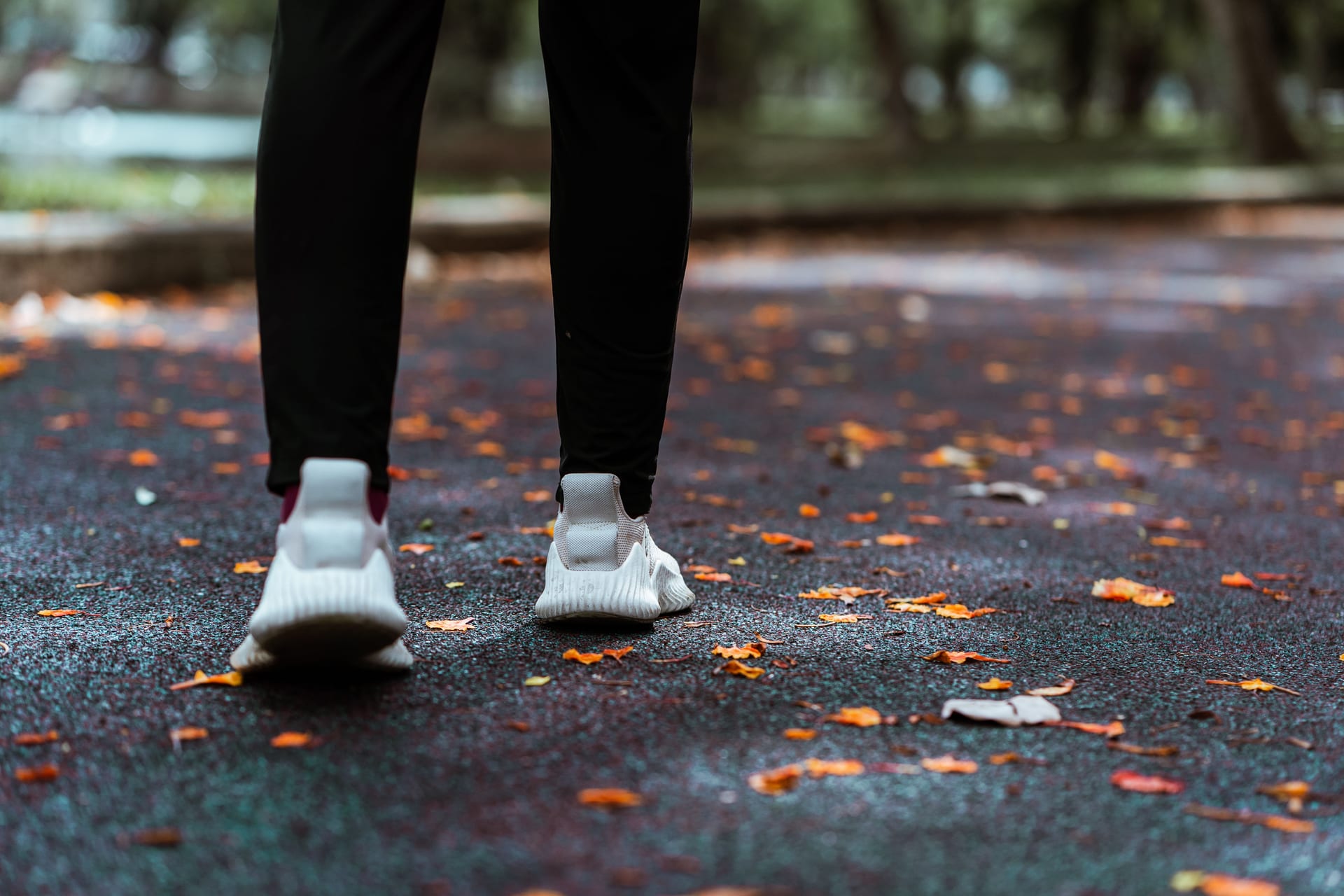 Una persona con leggings y tenis deportivos camina sobre un sendero cubierto de hojas secas.