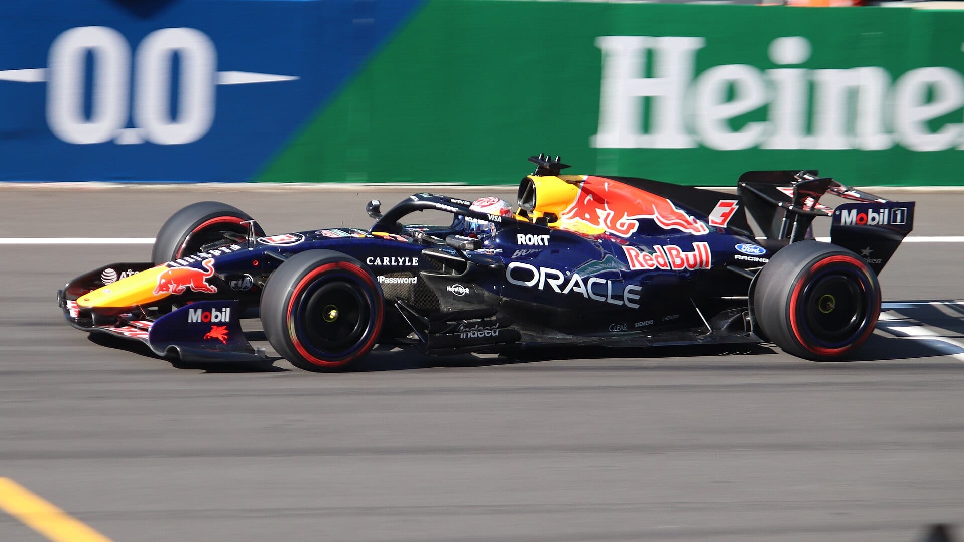 Monoplaza azul marino de Red Bull con logotipos de Oracle circula por una recta con anuncios de Heineken al fondo.