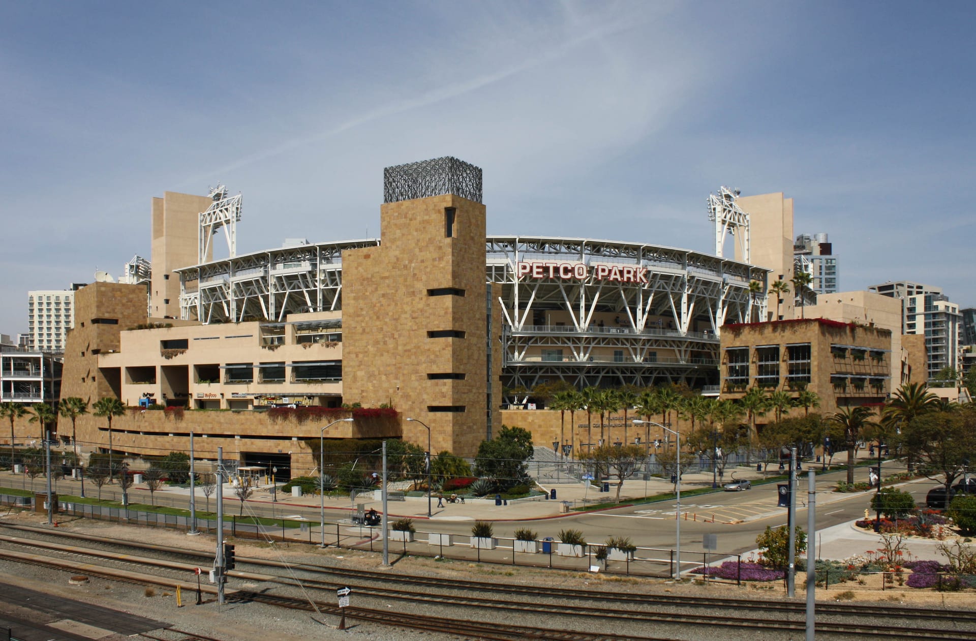 Fachada de piedra clara del Petco Park con el letrero del estadio y vías de tren en primer plano bajo un cielo despejado.