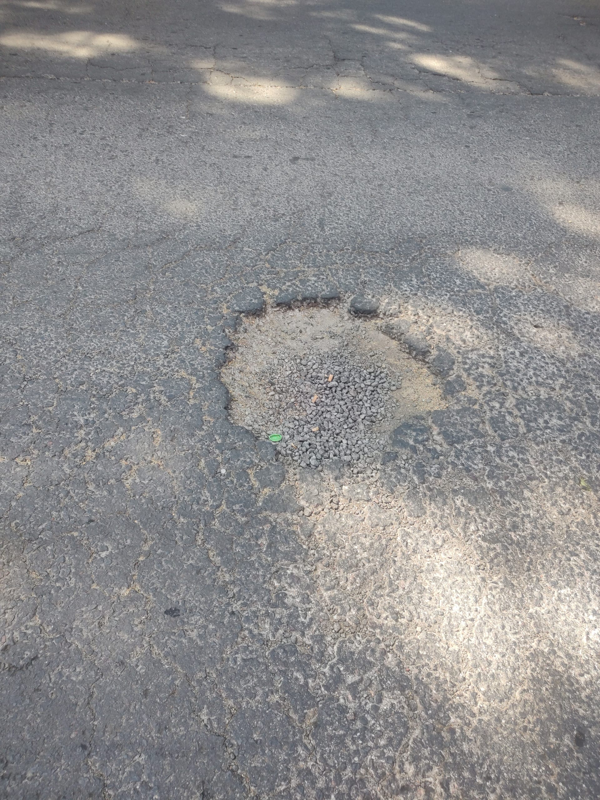 Un socavón parcialmente relleno con grava suelta en el pavimento de una calle de la Ciudad de México.