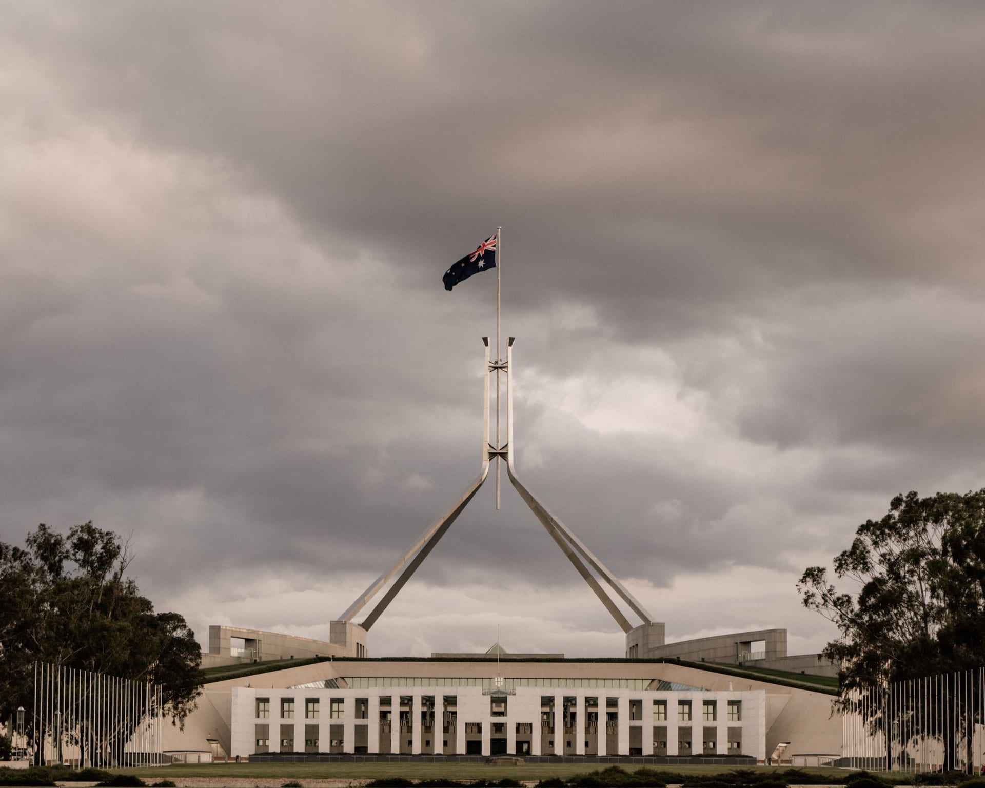 El asta bandera del Parlamento de Australia en Canberra, con la bandera nacional ondeando bajo un cielo nublado.
