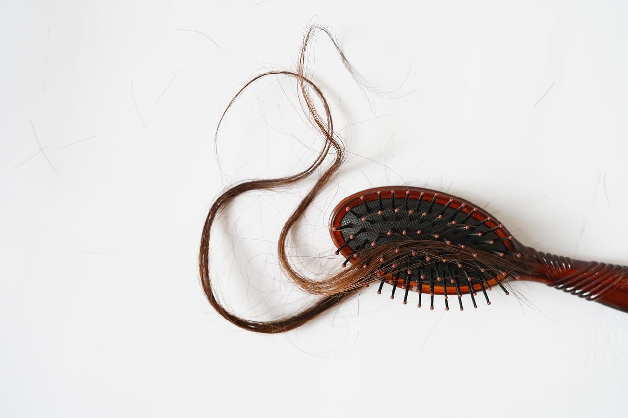 Un cepillo redondo para el cabello con mechones de pelo enredados entre las cerdas, sobre una superficie blanca.
