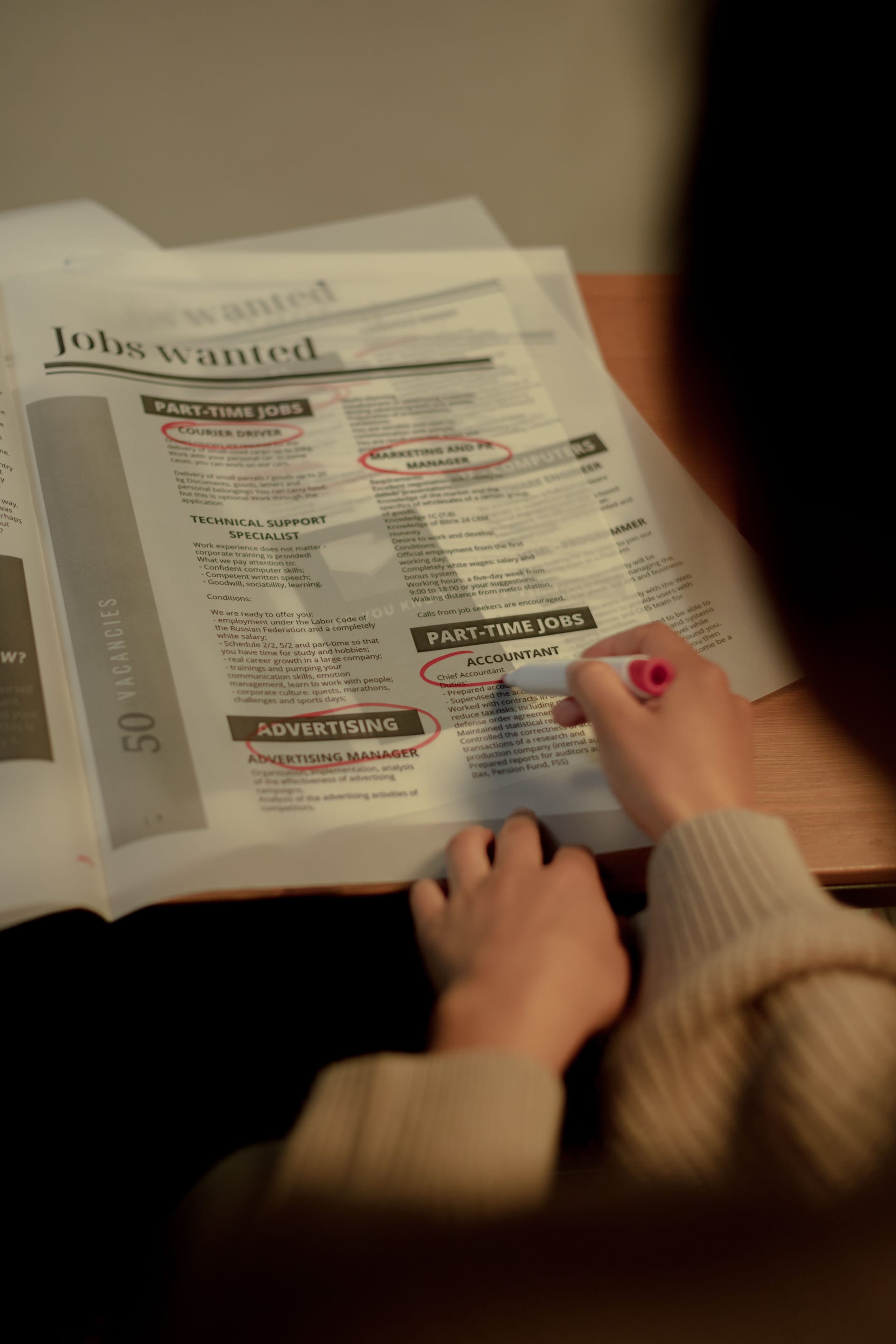 Una persona marca con pluma roja anuncios de empleo en la sección de clasificados de un periódico.