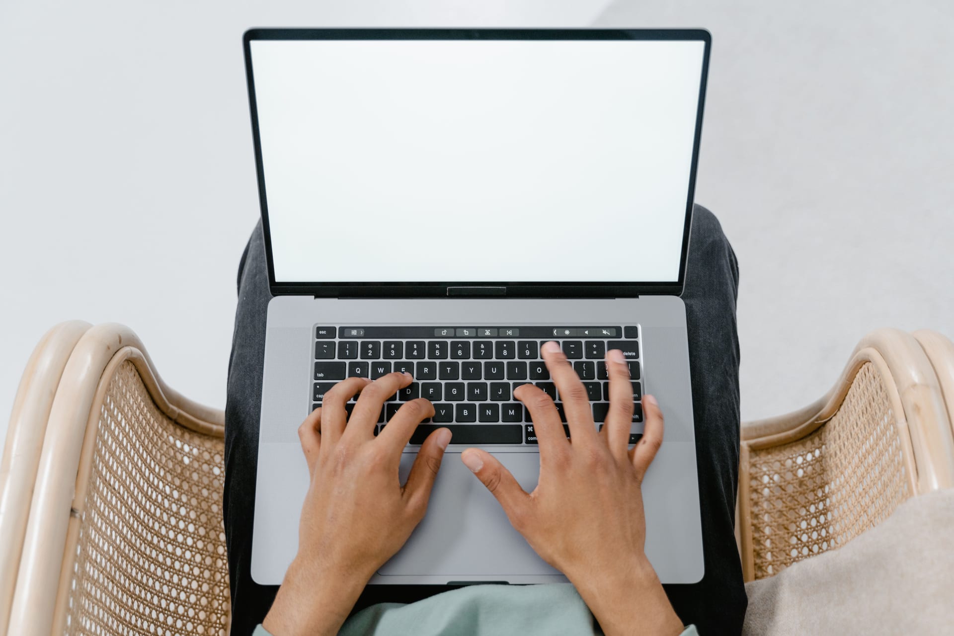 Vista aérea de unas manos escribiendo en el teclado de una laptop con la pantalla en blanco.