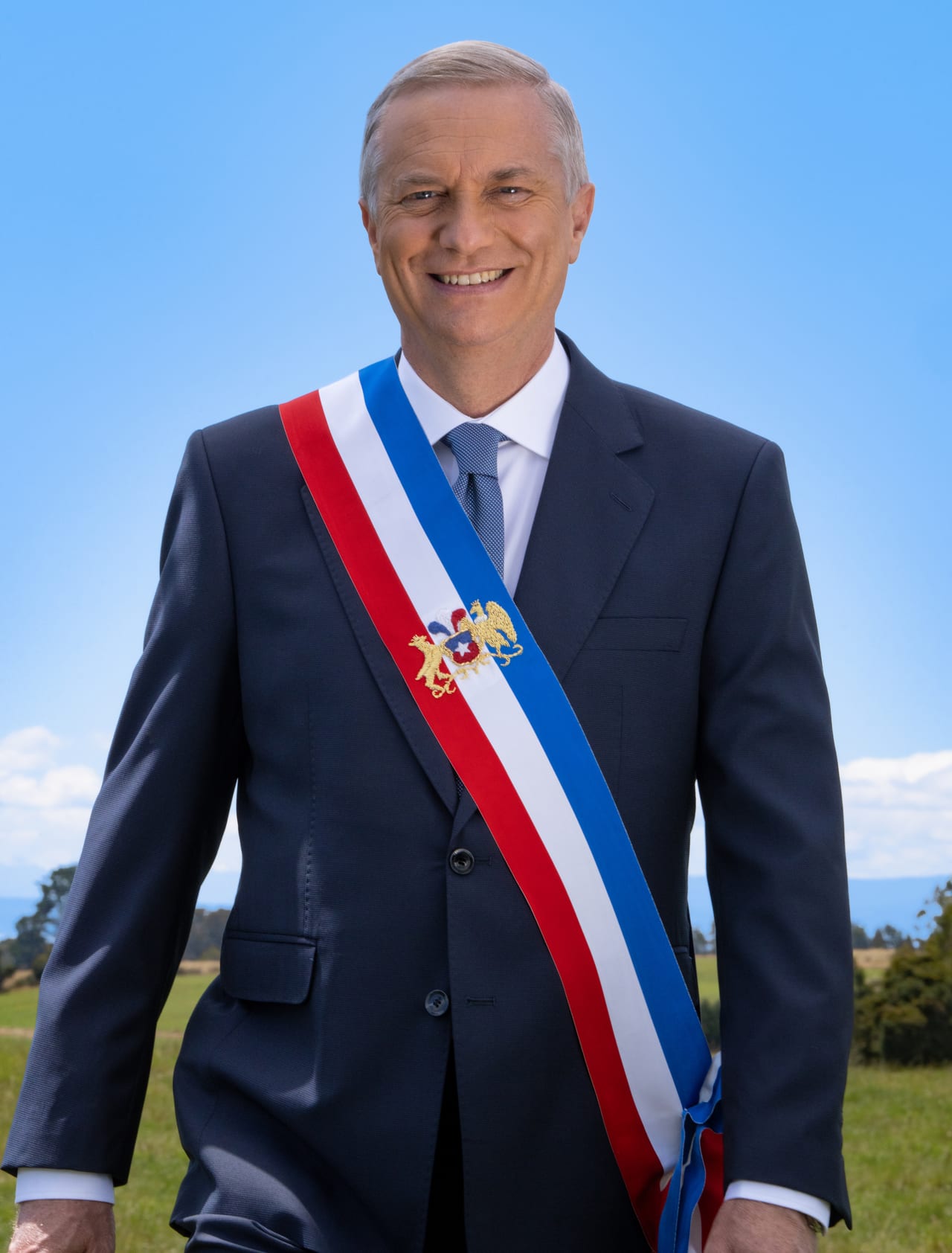 El presidente chileno José Antonio Kast sonríe con la banda presidencial cruzada al pecho, con cielo despejado y campo de fondo.