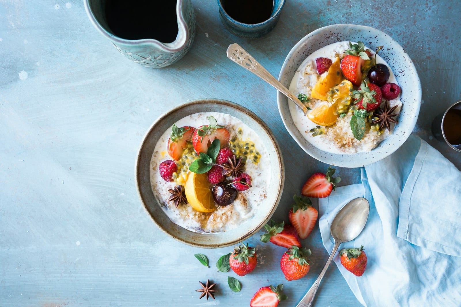Dos tazones de avena con fruta fresca, vistos desde arriba sobre una mesa azul.