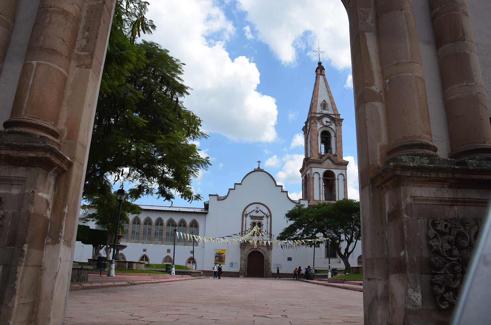 Fachada blanca y torre del templo de Jacona, Michoacán, vista desde un pórtico de piedra.