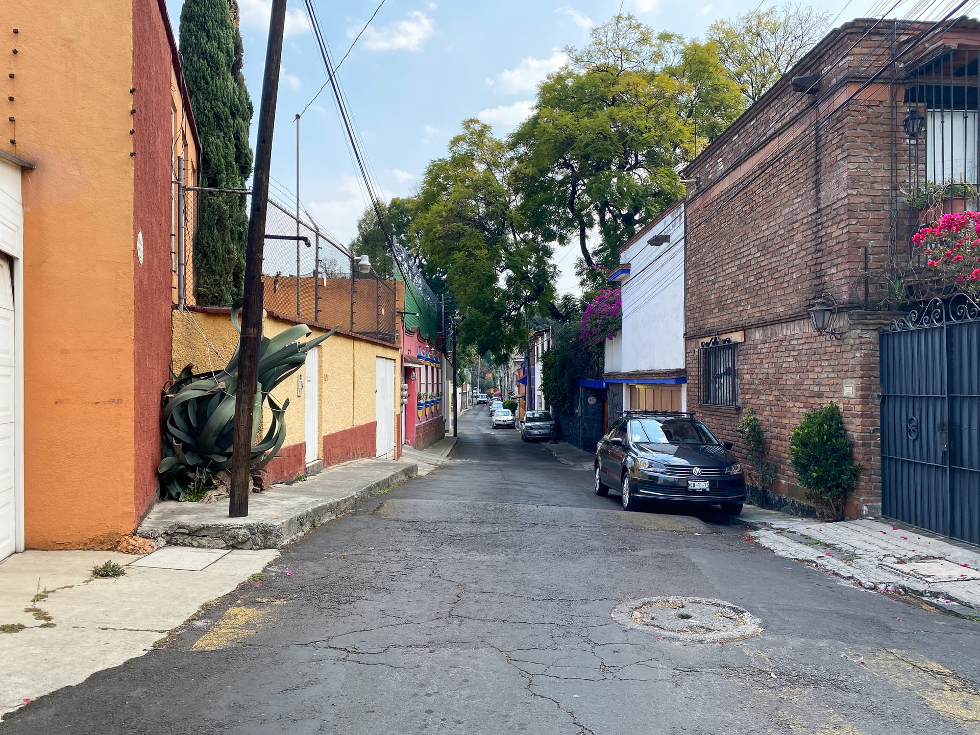 Calle empedrada de un barrio con casas de un piso pintadas de naranja y blanco, autos estacionados y árboles al fondo.