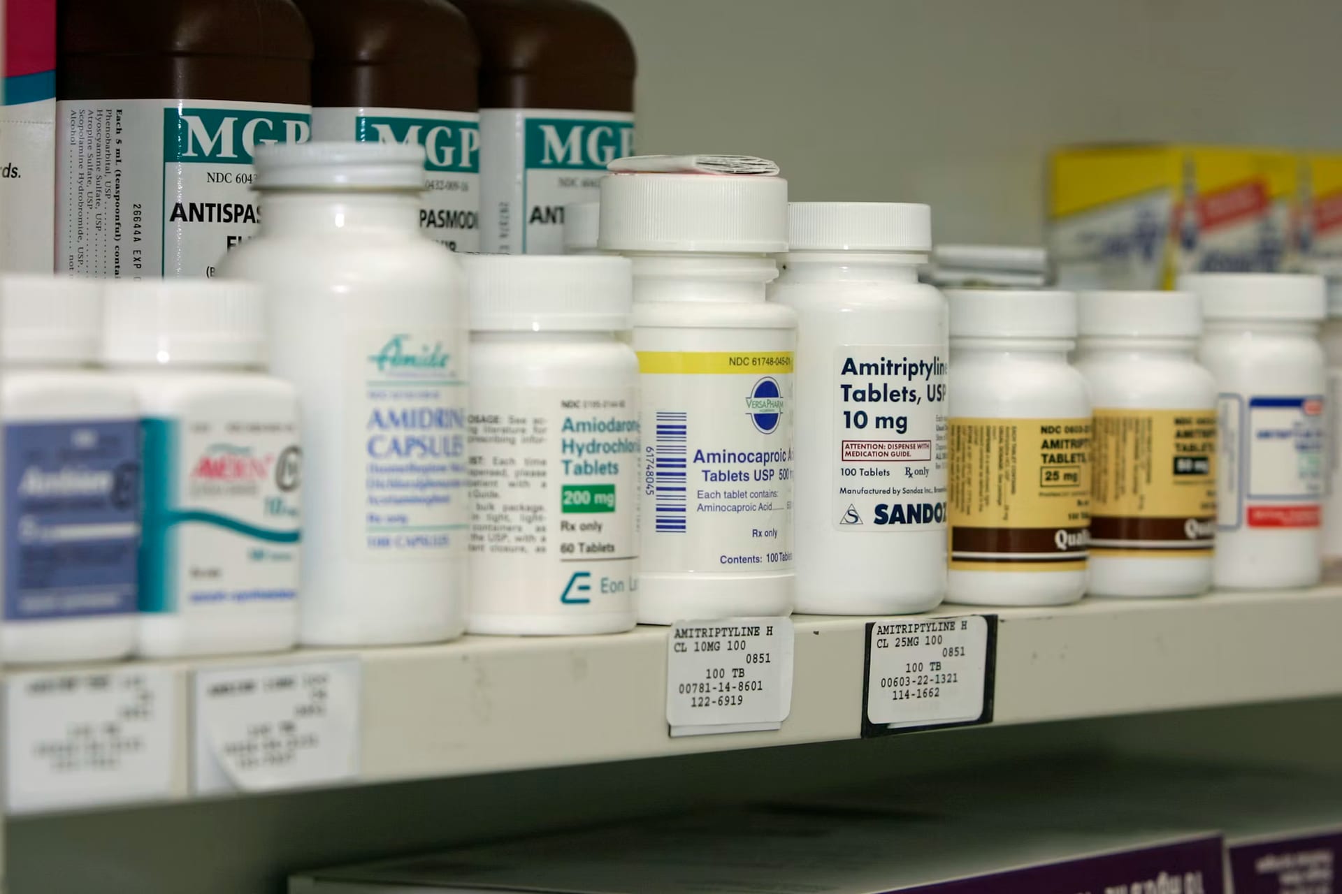 Un anaquel de farmacia con hileras de frascos y cajas de medicamentos ordenados.