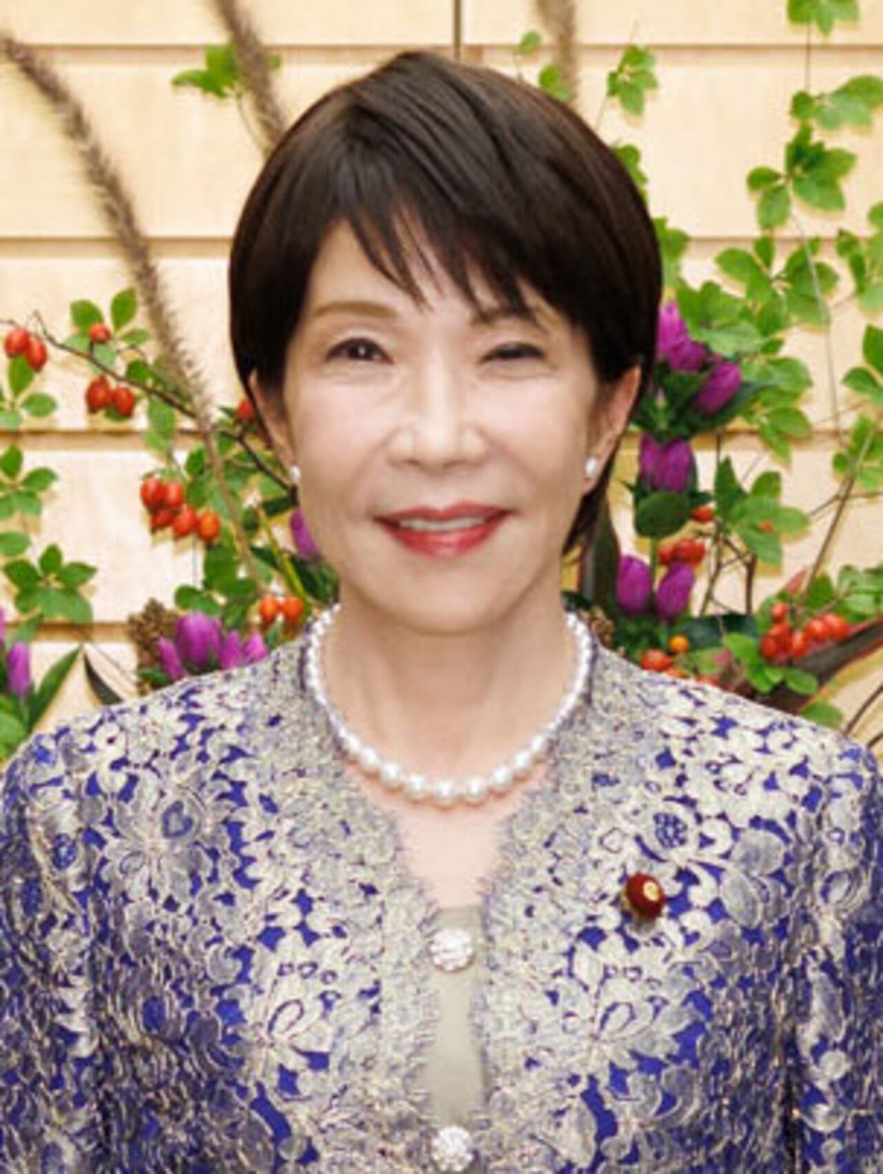 Retrato de la primera ministra japonesa Sanae Takaichi, con traje formal de gala, sonriendo ante un arreglo floral.