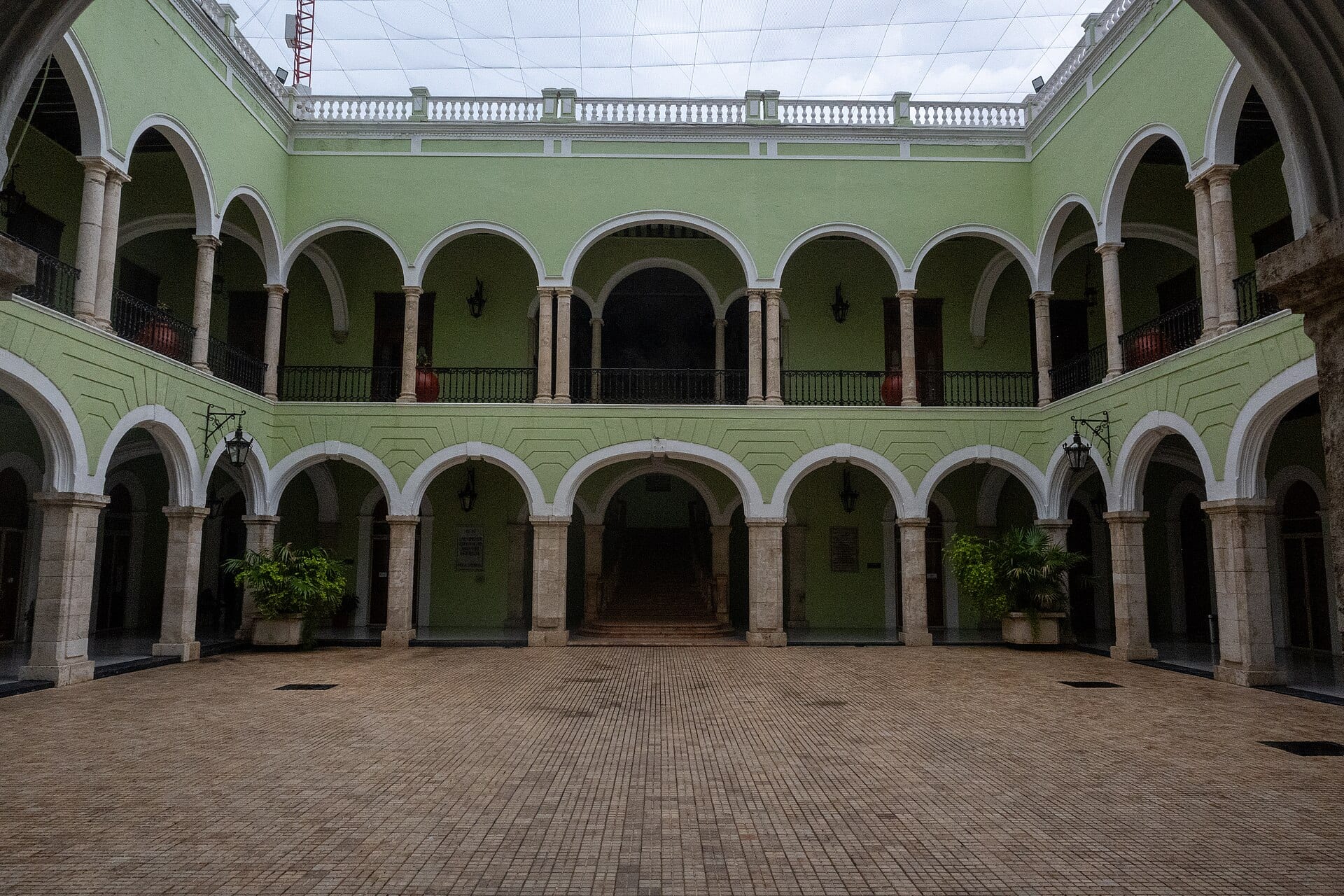Patio interior del Palacio de Gobierno de Yucatán, con arcadas de dos niveles pintadas de verde y piso de piedra.