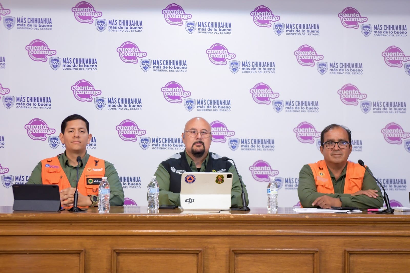 Tres funcionarios con chalecos de Protección Civil sentados en una mesa durante una rueda de prensa, con un fondo institucional del Gobierno del Estado de Chihuahua.