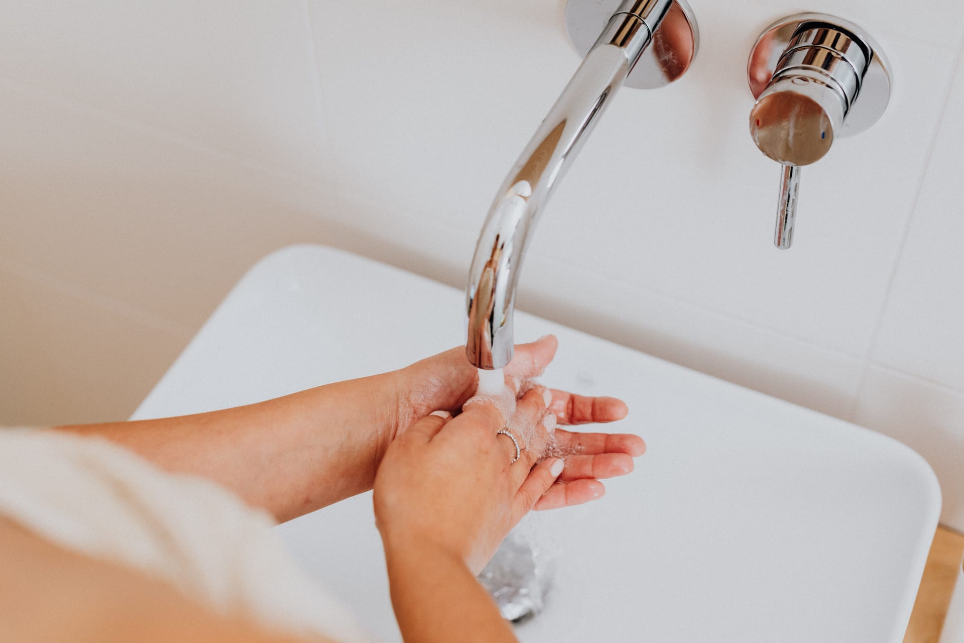 Un grifo de baño montado en la pared deja correr agua sobre un par de manos que se juntan bajo el chorro.