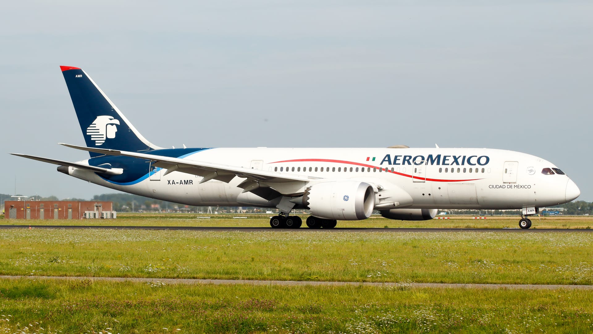 Un avión Boeing 787 de Aeroméxico con librea azul marino y roja rodando en pista, con el fuselaje completo visible contra un cielo nublado.