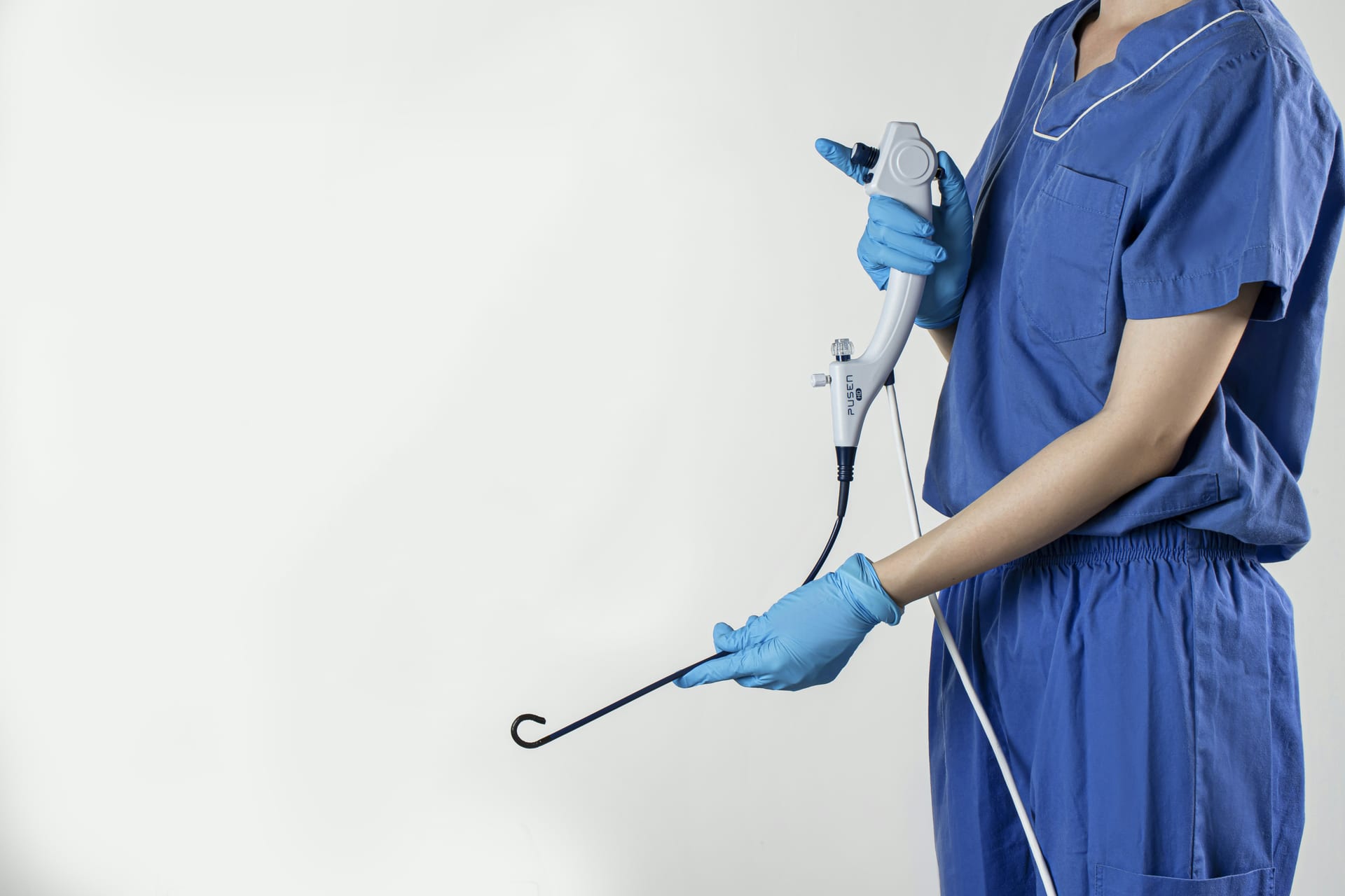 Una persona con guantes quirúrgicos azules sostiene un endoscopio flexible con la punta curvada hacia arriba.