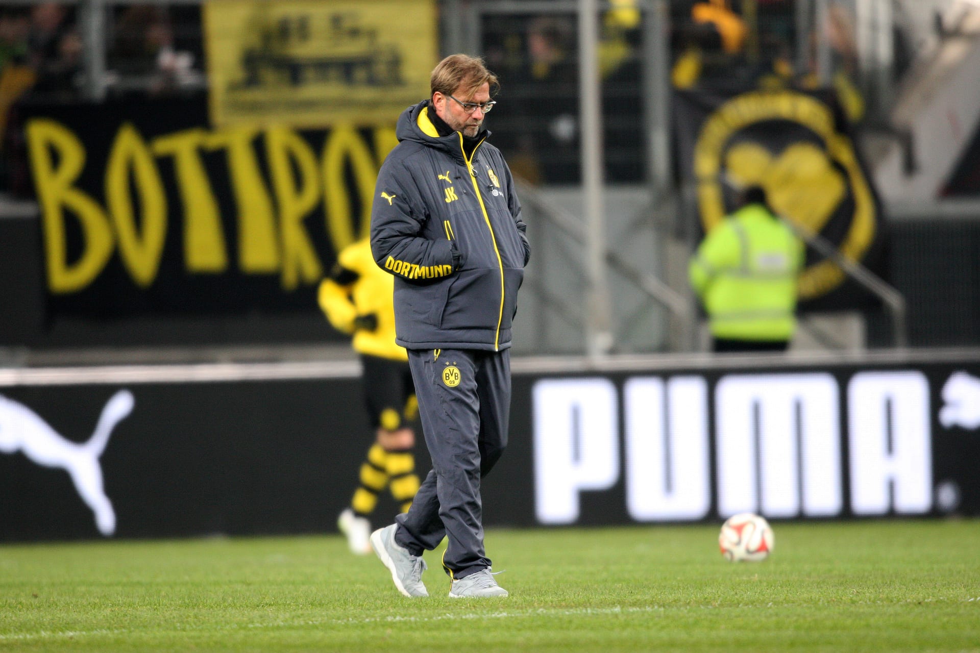 Jürgen Klopp camina con la mirada baja por una cancha de futbol, vestido con ropa deportiva oscura con las iniciales JK en la manga, en una imagen de archivo de su etapa como entrenador de club.