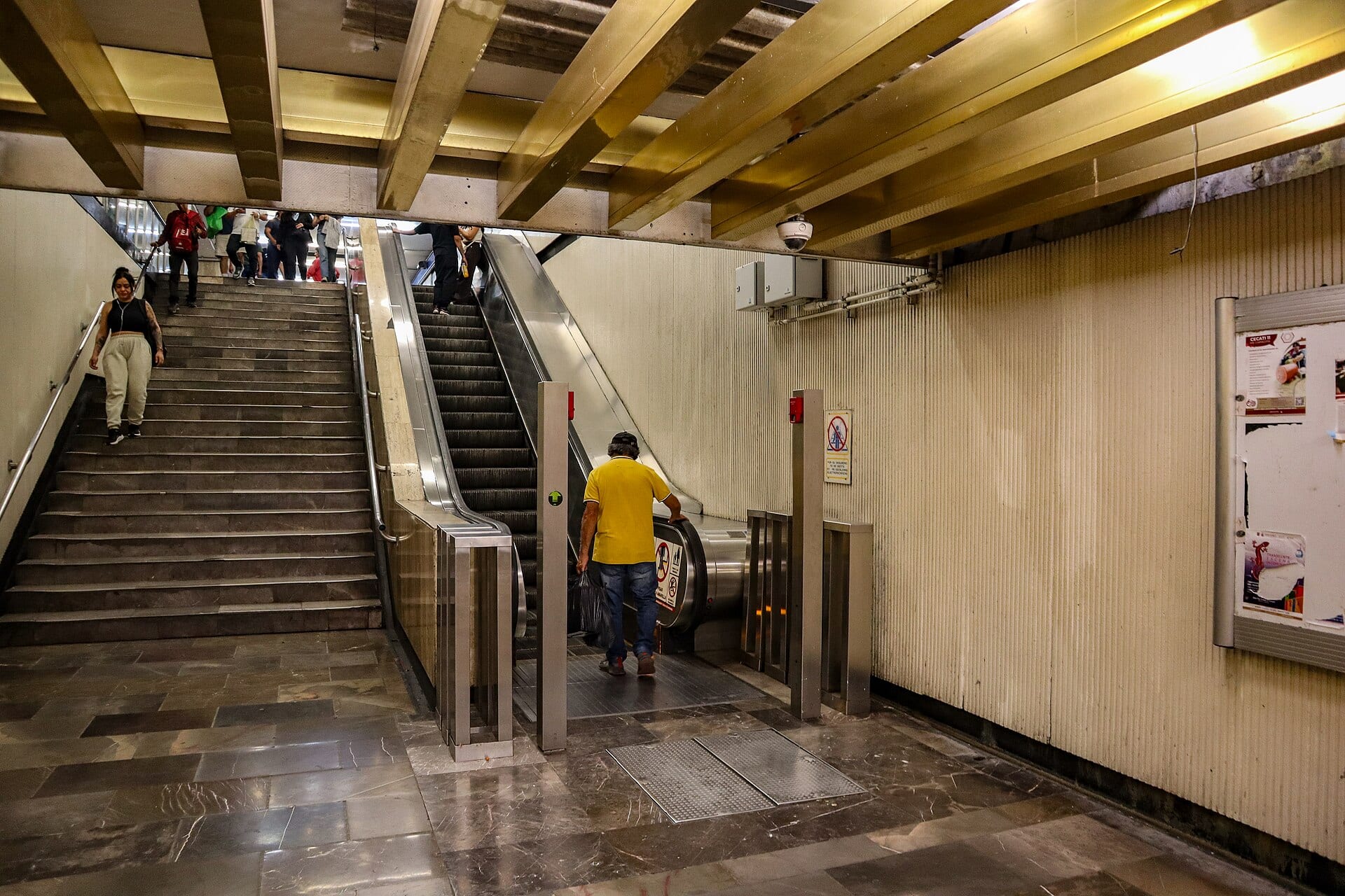 Un hombre con bolsa de mano baja por una escalera eléctrica mientras otros pasajeros usan la de junto en una estación del Metro.